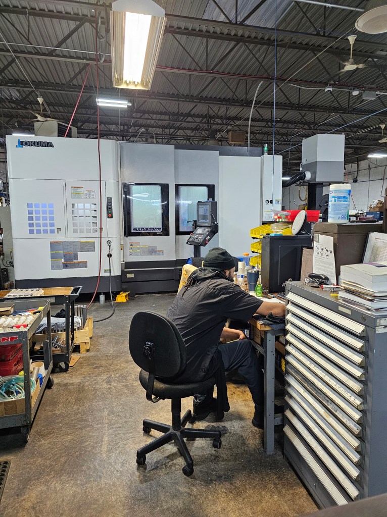 A man at a desk with a large CNC machine behind him.