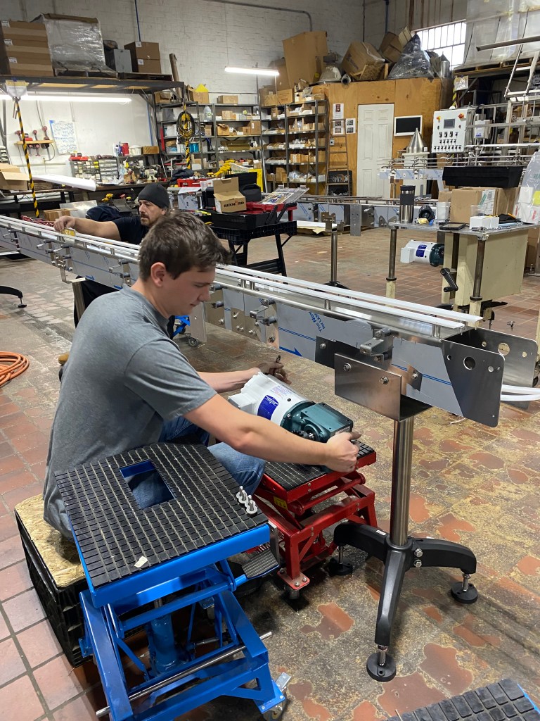 A man building a stainless steel conveyor in a machine shop.