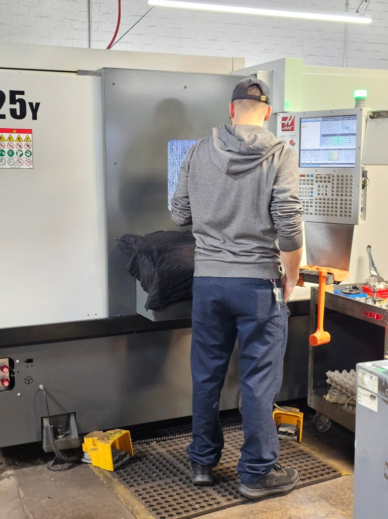 A man looking through the window of a CNC. There's water on the inside of the glass as it makes a part.