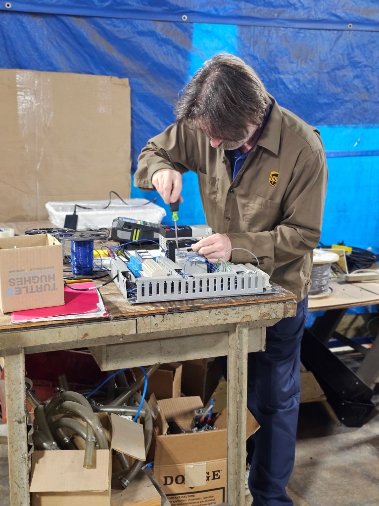 A man putting together a control box with a screwdriver in a machine shop.